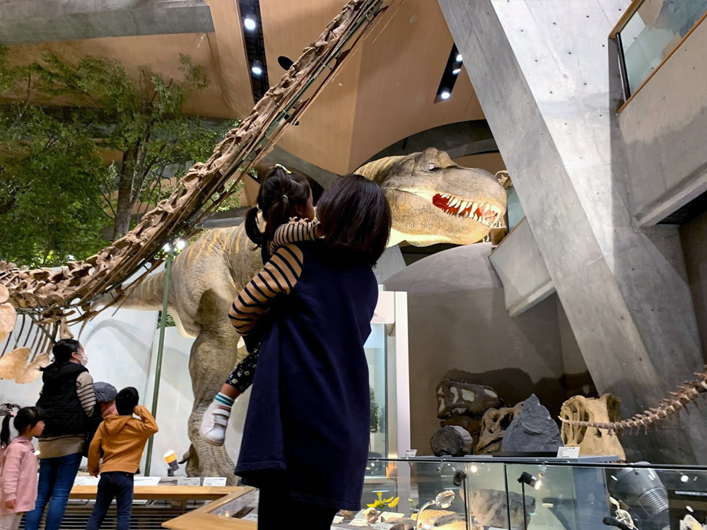 群馬県自然史博物館のティラノサウルスの動く模型前で母が娘を抱っこ