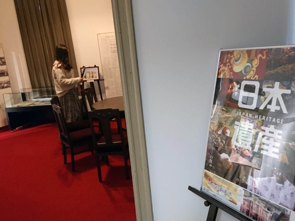 絹撚記念館を見学している彼女を日本遺産ポスター越しに撮影