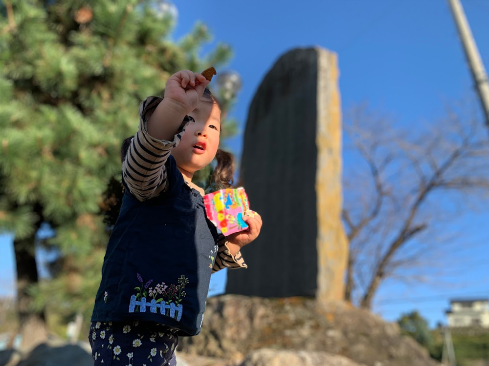 甘楽社小幡組由来碑前の看板前でお菓子を持つ娘
